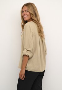 Beige losse blouse van zachte stof, met opgerolde mouwen, een ontspannen silhouet en een rugplooi.