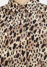 Blusa con stampa leopardata in tonalità di marrone, beige e nero. Presenta un colletto e chiusura con bottoni, realizzata in tessuto liscio e morbido.