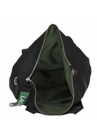 Sac de sport noir avec intérieur vert, fermeture éclair argentée ouverte et bandoulière verte étiquetée "LACOS", montré vide en vue de dessus.