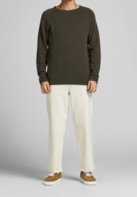 Olivgrüner Strickpullover mit langen Ärmeln und rundem Ausschnitt, kombiniert mit off-white weiten Hosen und hellbraunen Sneakers mit weißen Sohlen.