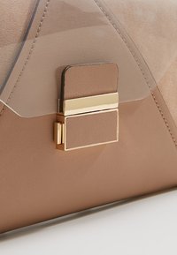 Gros plan d'un fermoir de sac à main en cuir beige avec une serrure rectangulaire en métal doré, un rabat recouvert de cuir et des détails de couture.