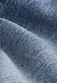 Denim-kangas sinisissä sävyissä, jossa on teksturoitu kudonta. Sisältää vaihtelevia sinisen sävyjä, luoden hienovaraisen kuviokankaan ja sileän pinnan.
