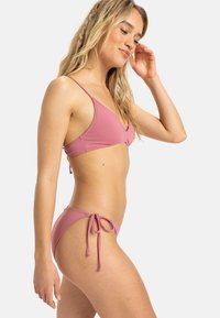 Ružový bikiny set s trojuholníkovým topom s nastaviteľnými ramienkami a bokovým viazaním, vyrobený z hladkej a elastickej látky.