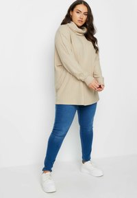 Beige ribbad polotröja med långa ärmar, tillsammans med blå smala jeans och vita sneakers. Slät textur och avslappnad passform.