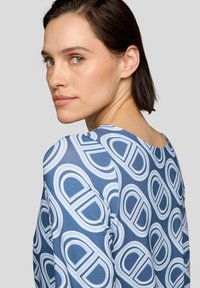 Langärmliges Oberteil in Blau mit einem sich wiederholenden weißen geometrischen Muster. Glatte Textur mit rundem Ausschnitt und taillierter Silhouette.