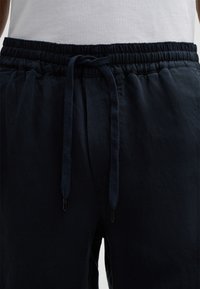 Pantaloni jogger blu navy con vita regolabile. Tessuto in cotone morbido, vestibilità rilassata e texture sottile. Presentano una vita elastica e lacci regolabili.