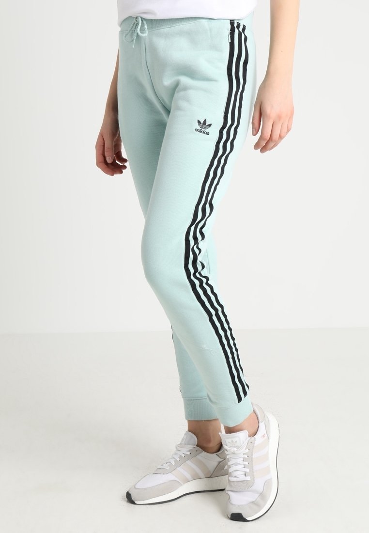 Světle modré joggingové kalhoty s černými bočními pruhy a elastickým pasem, které mají štíhlý střih a jemnou texturu. Stylizováno s bílými sportovními botami.