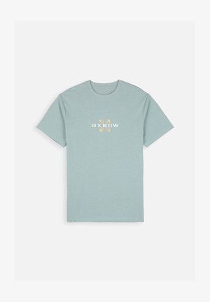 T-shirt bleu clair à manches courtes. Présente un logo Oxbow blanc et jaune sur le devant. Fabriqué en tissu doux avec un col rond.