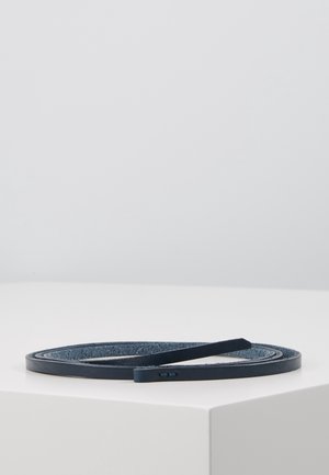 Smal mørkeblå læderbælte rullet sammen på hvid overflade med synlige syninger langs kanterne og tekstureret inderside.