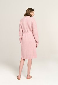 Rosa gestrickte Strickjacke mit Taillenknoten, langen Ärmeln und geripptem Saum. Weiche Textur, knielang und mit lockerer Passform.