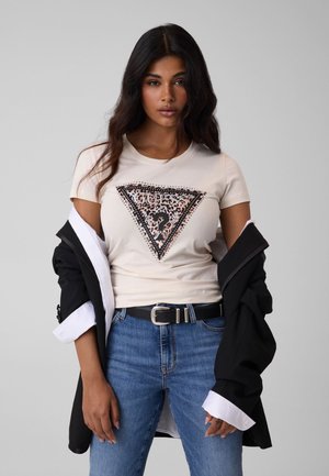 Mujer con una camiseta beige clara con un diseño de triángulo con estampado de leopardo, vaqueros azules y una chaqueta negra sobre los hombros.