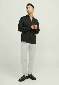 Black button-up shirt with long sleeves, paired with light gray pants and black shoes. Fabric appears textured and lightweight.
