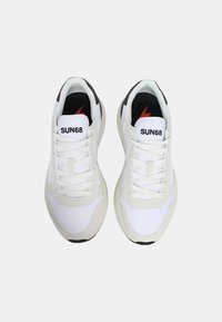 Zapatillas deportivas blancas con un upper de cuero liso y malla, cordones planos, acentos en negro y rojo, y una suela de goma texturizada.