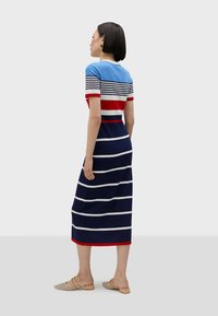 Randig stickad klänning i blått, rött och marinblått. Korta ärmar, rundad halsringning, figursydd midja och en lång, flödande kjol med horisontella ränder.