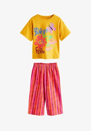 Sárga rövid ujjú ing színes "Rio de Janeiro Fesztivál" nyomattal, rózsaszín, narancs és piros csíkos, gumis derekú nadrággal párosítva.