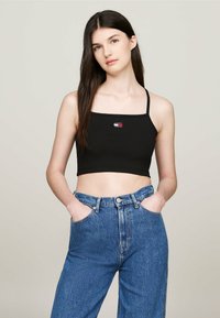 Top corto nero a coste con spalline sottili, caratterizzato da una piccola etichetta con logo multicolore. Abbinato a jeans in denim blu a vita alta.