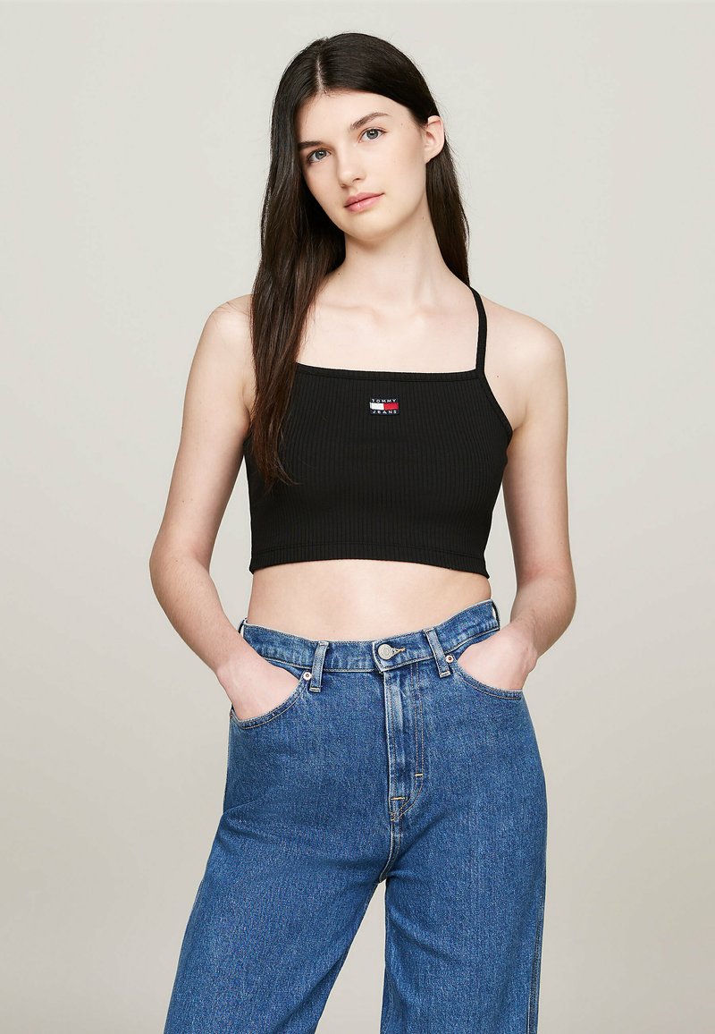 Top corto nero a coste con spalline sottili, caratterizzato da una piccola etichetta con logo multicolore. Abbinato a jeans in denim blu a vita alta.