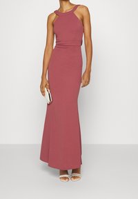Enganliegendes burgunderfarbenes Kleid mit hohem Ausschnitt, ärmellosem Design und ausgestelltem Rock. Kombiniert mit weißen, offenen High Heels und einer kleinen Clutch.