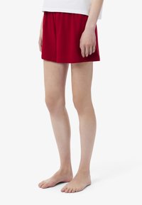Pantaloni corti rossi in cotone con vita elasticizzata, caratterizzati da una vestibilità comoda e una texture liscia, posizionati sopra il ginocchio.
