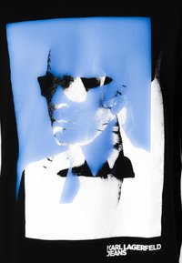 Camiseta negra con un estampado gráfico azul de una cara con gafas de sol, con acentos en blanco y el texto "KARL LAGERFELD JEANS" en la parte inferior.