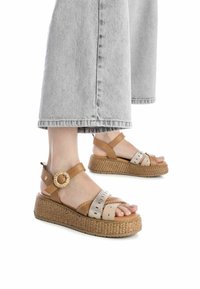 Sandalias de cuña marrones y beige con textura trenzada, tiras de cuero, acento circular en el tobillo y diseño de punta descubierta.