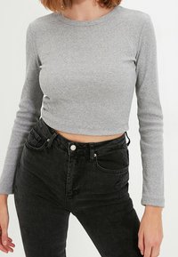 Grå ruggad långärmad crop top tillsammans med h�ögmidjade svarta jeans i denim med framfickor och synlig knappgylf.