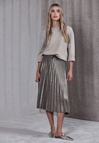 Ljusgrå stickad tröja med trekvartslånga ärmar, tillsammans med en metallisk plisserad kjol i silvertoner. Skorna är reflexiva ballerinaskor.