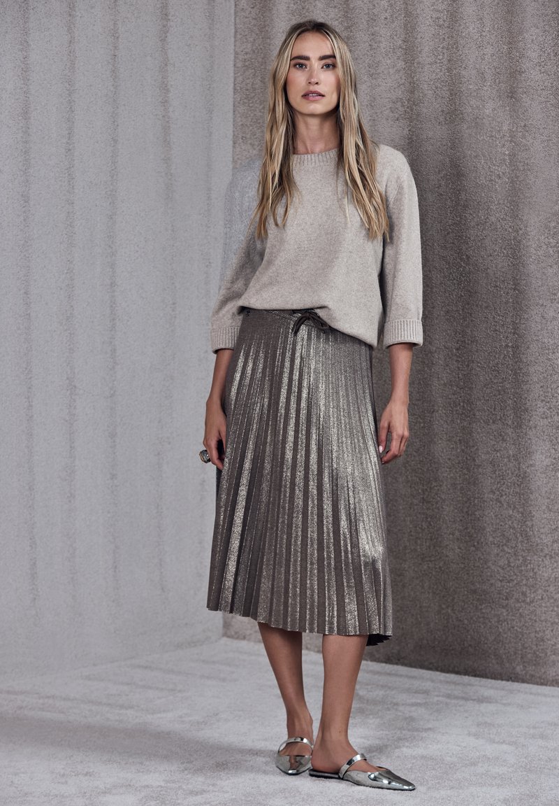 Ljusgrå stickad tröja med trekvartslånga ärmar, tillsammans med en metallisk plisserad kjol i silvertoner. Skorna är reflexiva ballerinaskor.