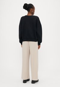 Sweatshirt preta de corte folgado, com punhos e bainha canelados, combinada com calças largas creme e botas pretas robustas. Fundo neutro.