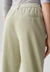 Pantaloni in corda verde chiaro con texture a costine verticali, fascia elastica in vita e tasche posteriori, mostrati da un angolo laterale.