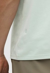 Gai piparmētru zaļas krāsas īsām piedurknēm krekls ar apaļu dekoltē, gluda kokvilnas tekstūra un neliels logo akcents pie apakšmalas.