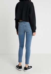 Sweat-shirt noir court, jean skinny bleu clair, ourlet effiloché, baskets noires. Accent sur un design décontracté et une silhouette ajustée.