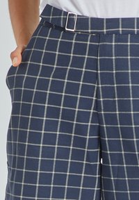 Pantalones de cuadros en navy con un patrón de rejilla en beige claro. Tienen una cintura con cinturón y bolsillos laterales con una textura suave.