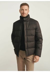 Czarna kurtka puchowa z wysokim kołnierzem i zapięciem na zatrzaski, z pikowanym wzorem i subtelnym połyskiem. Nosi ją osoba w czarnym swetrze.