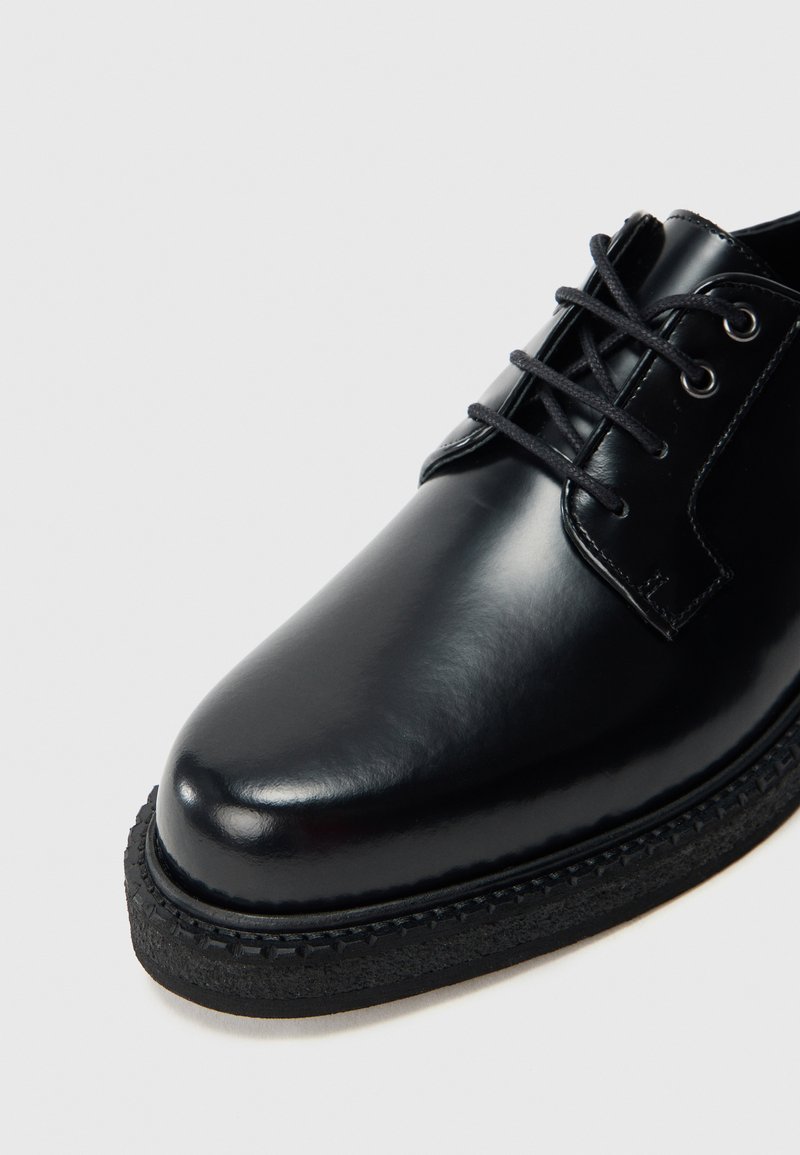 Black leather dress shoe with a polished finish, rounded toe, and contrasting textured rubber sole. Features lace-up closure and stitched accents.