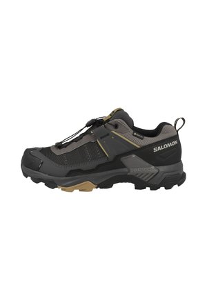 Scarpa da trekking outdoor nera e grigia con accenti beige, suola robusta, sistema di allacciatura rapida e marchio Salomon sul lato.