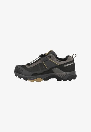 Zapato de senderismo para exteriores en negro y gris con acentos beige, con suela resistente, sistema de cordones rápidos y marca Salomon en el lateral.