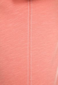 Tejido de coral claro con una sutil textura jaspeada, con una costura visible que corre verticalmente por el centro.