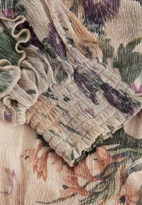 Kwiatowa tkanina z miękkiego, przezroczystego materiału z plisowaniem i lśniącymi nitkami. Zawiera falbanki i marszczenie.