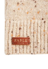 Pleteni volneni klobuk v kremni barvi s pridihi oranžne in rjave, ki ima teksturiran rebrast dizajn ter rjavo usnjeno oznako s potiskano napisom "FABLE ENGLAND."