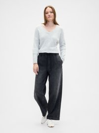 Suéter de punto suave en gris claro con escote en V y mangas largas, combinado con pantalones de mezclilla oscuros de corte holgado que tienen una cinturilla elástica.