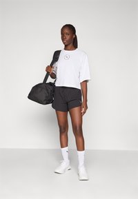 Valge lühike T-särk ringikujulise logoga, mustad sportlikud lühikesed püksid, valged pahkluuni sokid ja must spordikott; minimalistik stiil, igapäevane sobivus.
