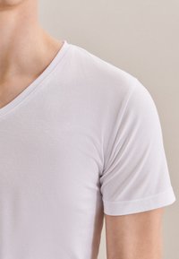 T-shirt bianco a maniche corte in tessuto morbido e leggero. Presenta un collo a V e risvolti sulle maniche, con una superficie liscia e senza texture.