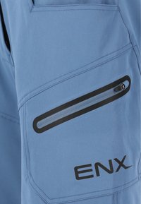 Hellblaue Cargo-Hose aus Stoff mit einer Reißverschlusstasche mit schwarzem Besatz, soliden Nähten und einem schwarzen "ENX"-Logo am Bein.