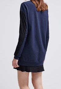 Navy sweatshirt with black sleeves, soft fabric, ribbed cuffs, and a relaxed fit. Paired with a pleated black skirt.