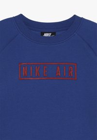 Blaues Sweatshirt mit geripptem Rundhalsausschnitt, Raglanärmeln und einem roten, bestickten "NIKE AIR"-Logo in einem rechteckigen Rahmen.