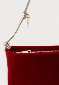 Červená sametová kabelka so zlatým zipsom a kovovým popruhom, ktorý obsahuje malú zlatú visačku s nápisom "FURLA".