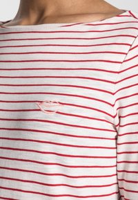 Maglietta a maniche lunghe a righe rosse e bianche in morbido tessuto, con scollatura a barca e un piccolo logo di labbra ricamato sul petto.
