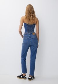 Haut corset en denim avec un dos froncé, associé à un jean taille haute à jambe droite bleu moyen, et des baskets noires à semelles beiges.