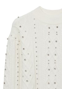 Weißer Strickpullover mit Kabelmuster, verziert mit dekorativen silbernen Nieten, die vertikal und horizontal über den Stoff angeordnet sind.